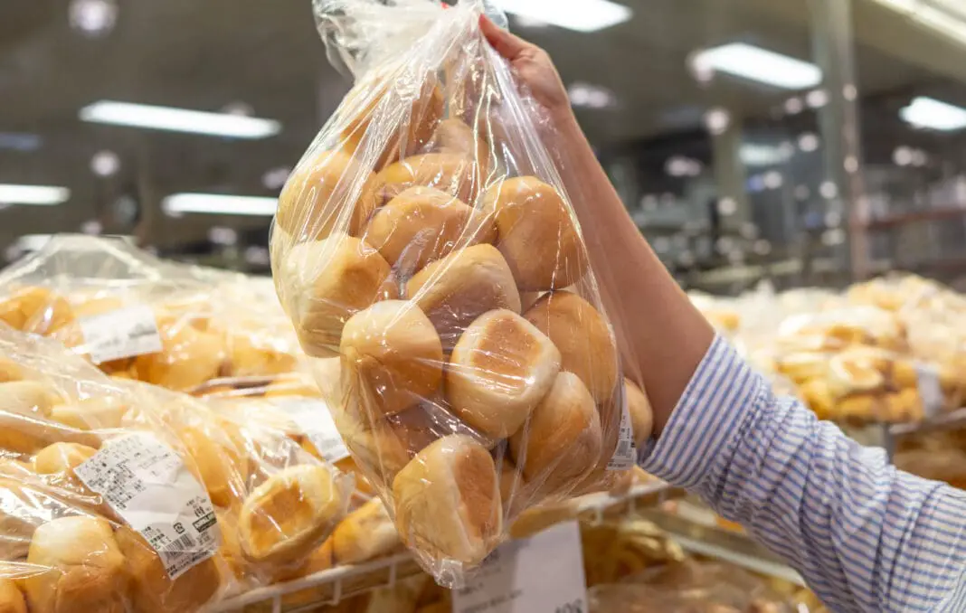 A shopper's hand getting a bag of Costco Dinner Rolls from the shelf