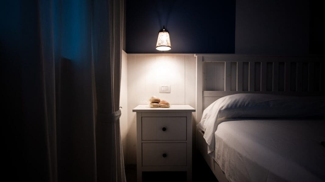A bedside lamp illuminates a nightstand next to a bed.