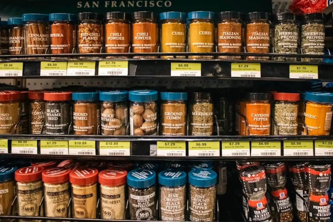 his is a close-up shot of a retail shelf displaying a wide variety of Morton & Bassett spices. The spices are packaged in small glass jars with labels indicating the type of spice and the brand, Morton & Bassett, with 