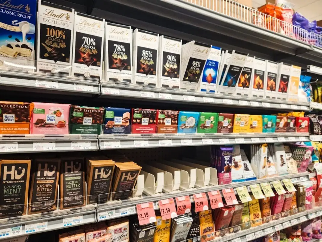 Grocery store shelves are neatly stocked with a variety of chocolate bars, featuring diverse brands, flavors, and packaging designs.