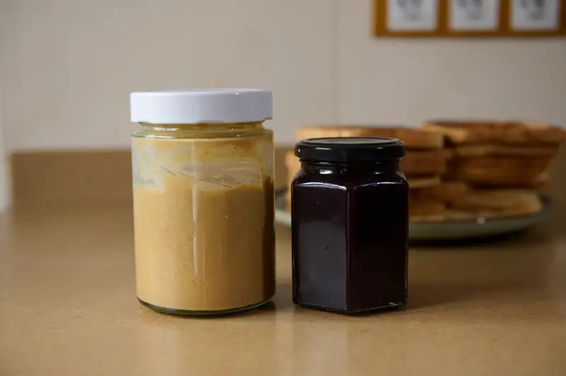 Peanut Butter And Jam Jars On Kitchen Counter With Pancake Stack In Background