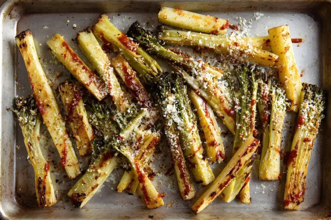 Parmesan roasted broccoli stem fries, pale gold and just softened on a plain steel baking sheet, with smoked paprika and grated parmesan cheese